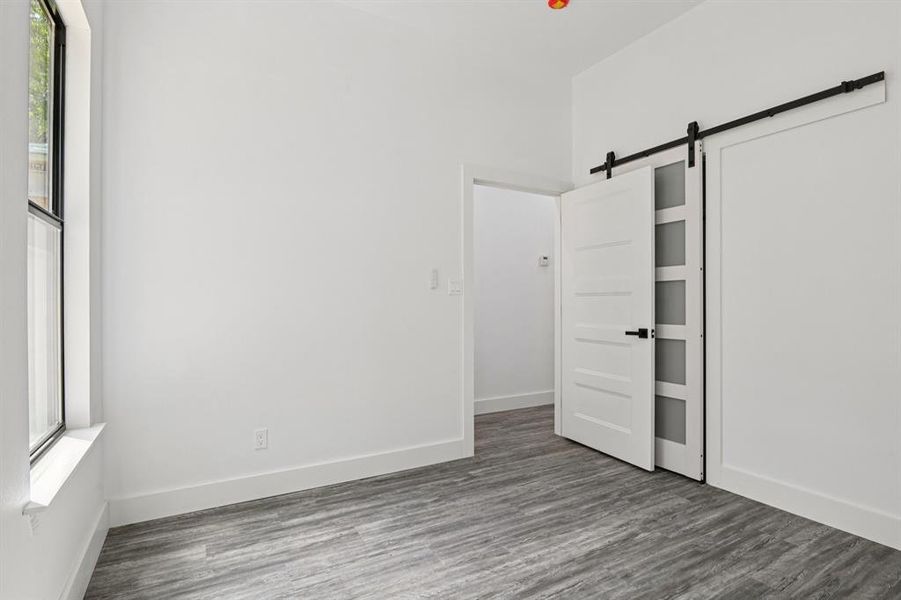 Unfurnished bedroom featuring a barn door and wood finished floors Unfurnished bedroom featuring a barn door and wood finished floors