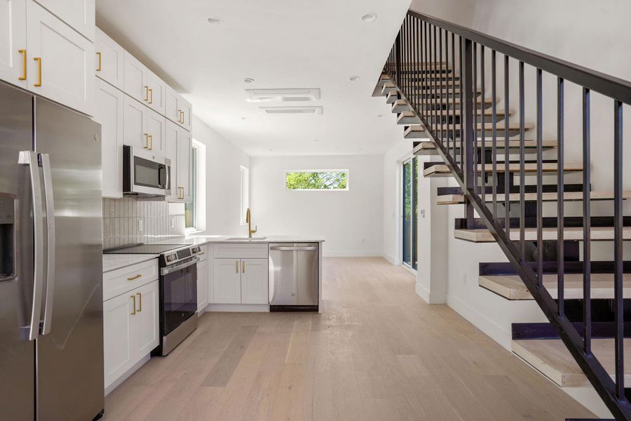 Kitchen with tasteful backsplash, baseboards, light wood-style flooring, stainless steel appliances, and a sink