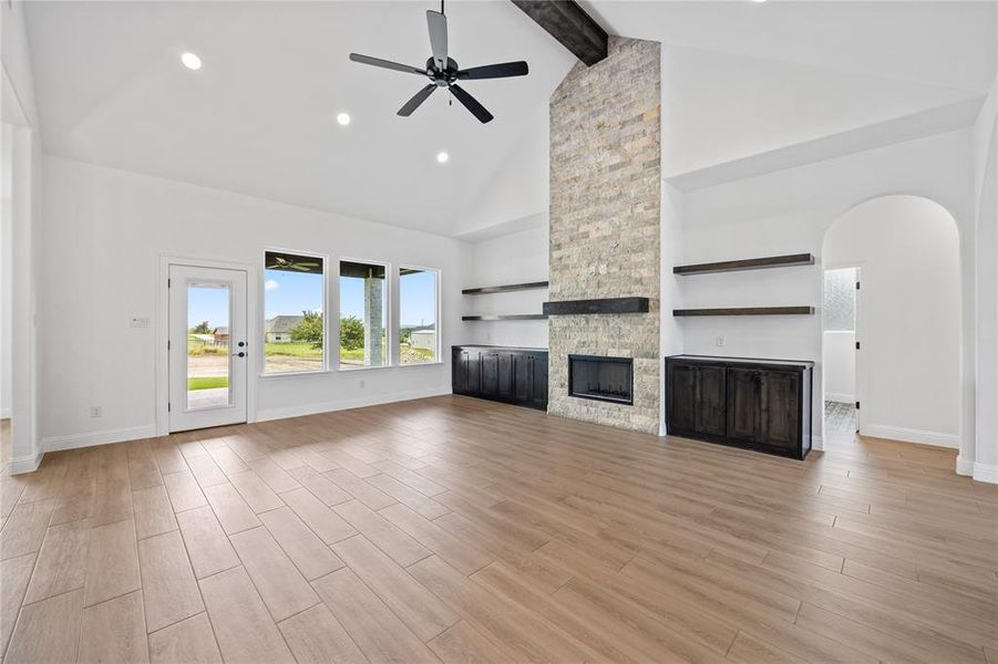 Unfurnished living room with beamed ceiling, high vaulted ceiling, a ceiling fan, light wood-type flooring, and arched walkways