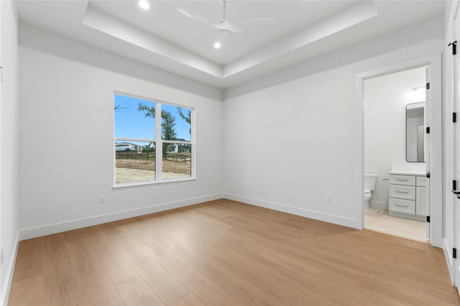 Unfurnished bedroom with light wood-style floors, a ceiling fan, connected bathroom, a tray ceiling, and recessed lighting