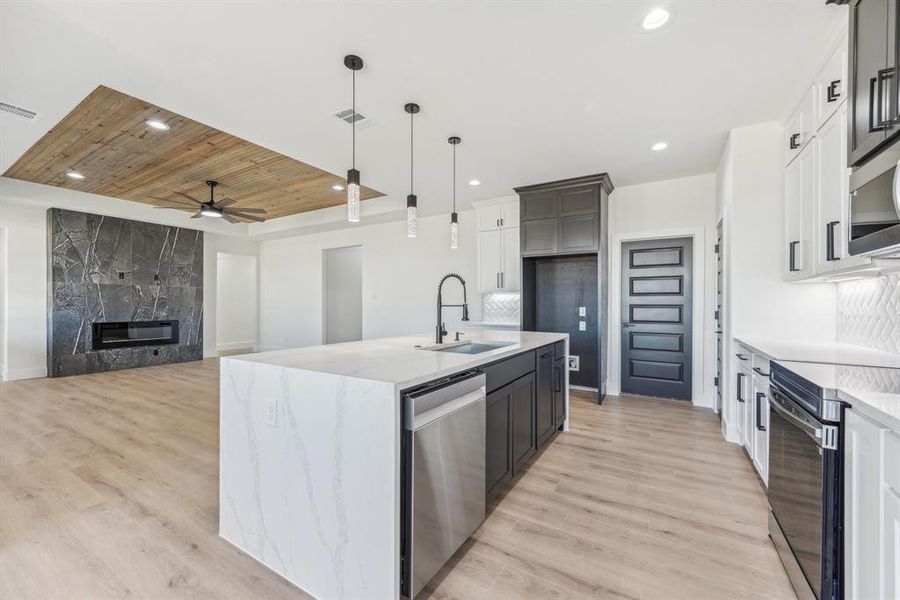 Kitchen with a kitchen island with sink, pendant lighting, stainless steel appliances, and light hardwood / wood-style flooring