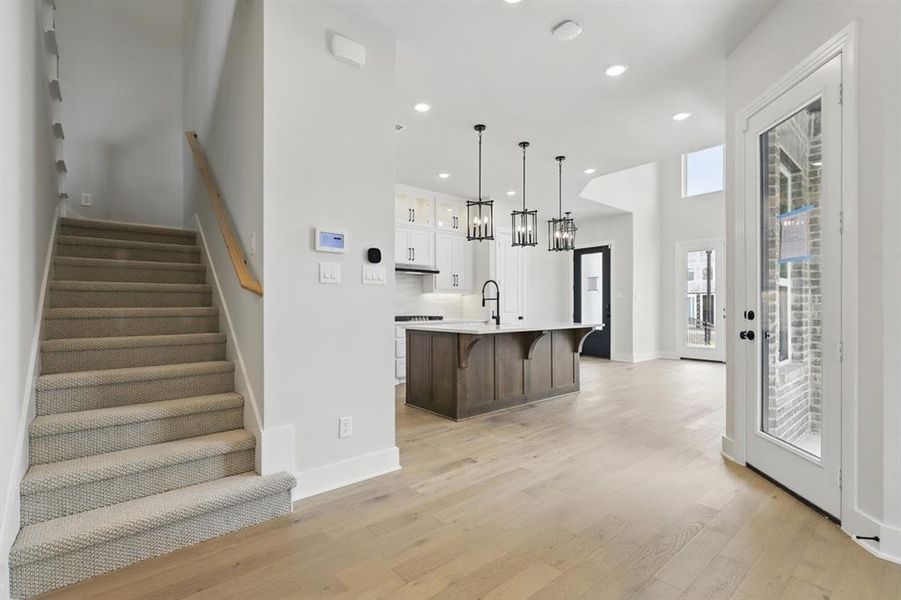 Kitchen featuring white cabinetry, glass insert cabinets, decorative light fixtures, recessed lighting, and an island with sink