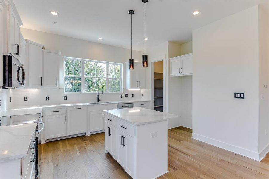 Kitchen with white cabinets, a kitchen island, light stone countertops, and light hardwood / wood-style floors