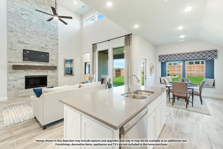 Open-concept kitchen with island sink, stone fireplace, high ceilings, and dining area with backyard views