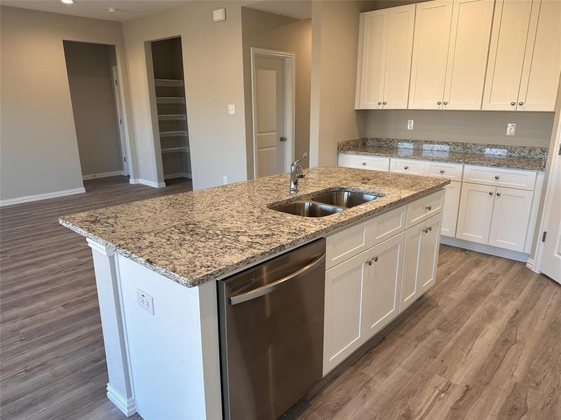 Kitchen featuring sink, dishwasher, hardwood / wood-style floors, white cabinetry, and an island with sink