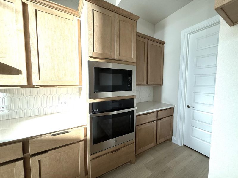 Kitchen with light countertops, oven, built in microwave, decorative backsplash, and light wood-style flooring