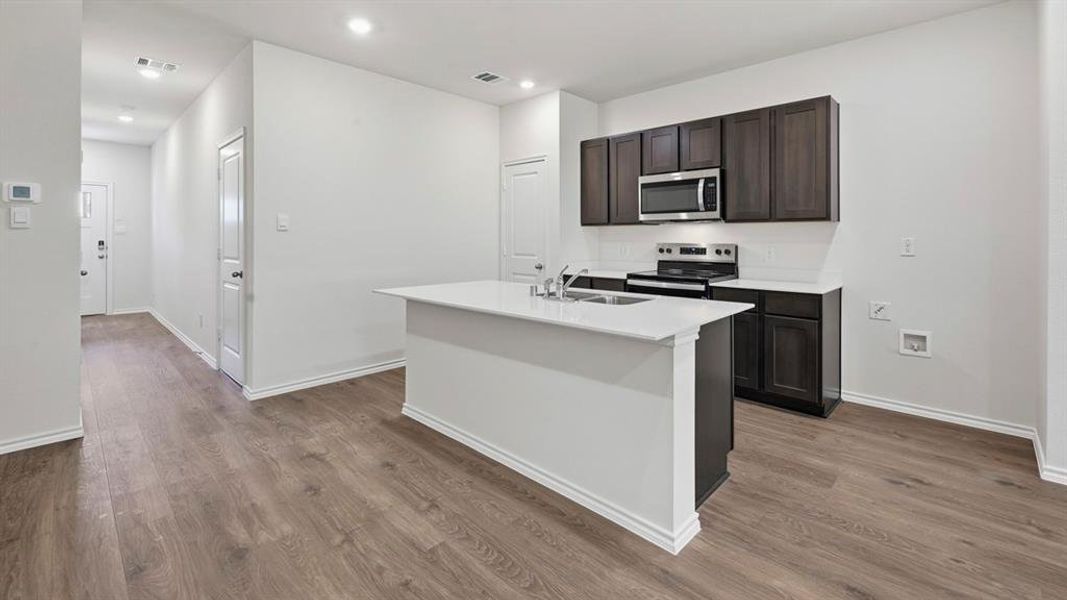 Kitchen with stainless steel appliances, a kitchen island with sink, dark brown cabinets, dark wood-type flooring, and recessed lighting