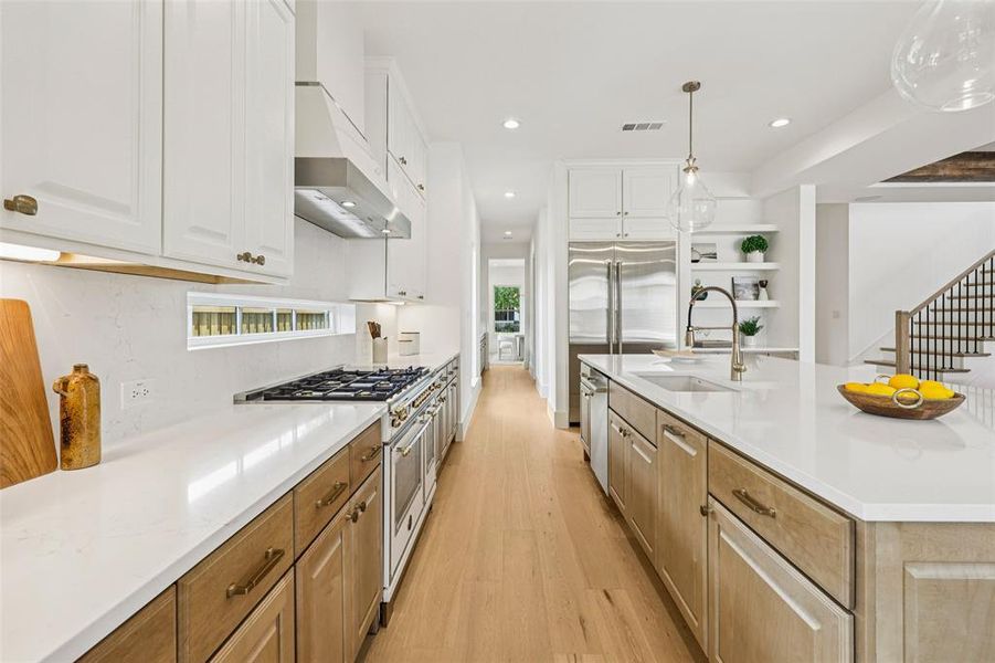 Modern kitchen featuring a gas range, dual-tone cabinetry, stainless steel appliances, a center island with a built-in sink, and light wood-finish flooring