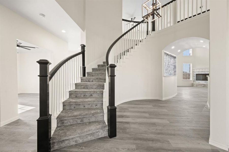 Stairs with a towering ceiling, arched walkways, a ceiling fan, a stone fireplace, and recessed lighting Stairs with a towering ceiling, arched walkways, a ceiling fan, a stone fireplace, and recessed lighting