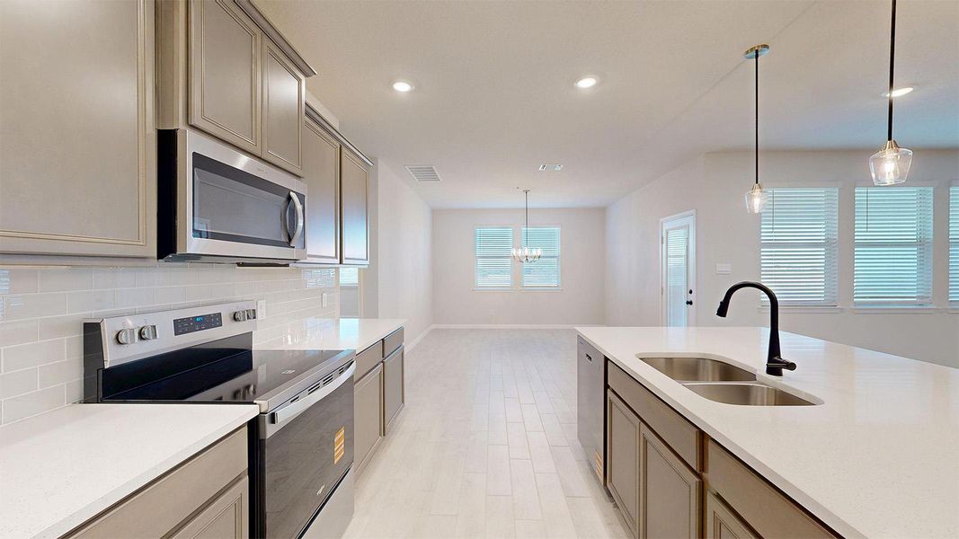 Kitchen with stainless steel appliances, light wood finished floors, tasteful backsplash, hanging lights, and light stone counters