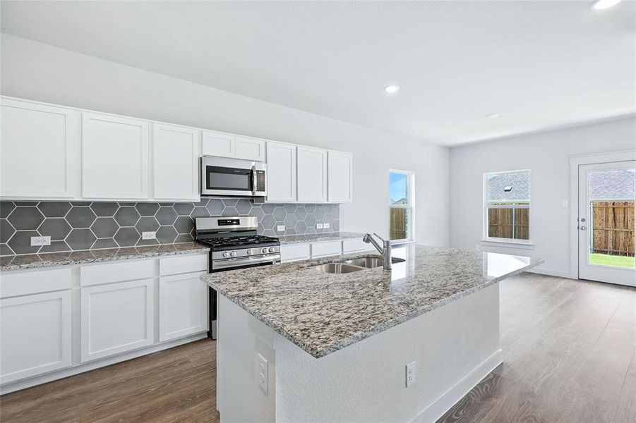 Kitchen featuring white cabinetry, backsplash, light stone counters, dark wood-style floors, and appliances with stainless steel finishes Kitchen featuring white cabinetry, backsplash, light stone counters, dark wood-style floors, and appliances with stainless steel finishes