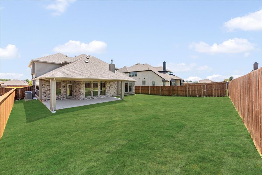 Brick home rear view with covered patio, large fenced backyard, and green lawn Brick home rear view with covered patio, large fenced backyard, and green lawn