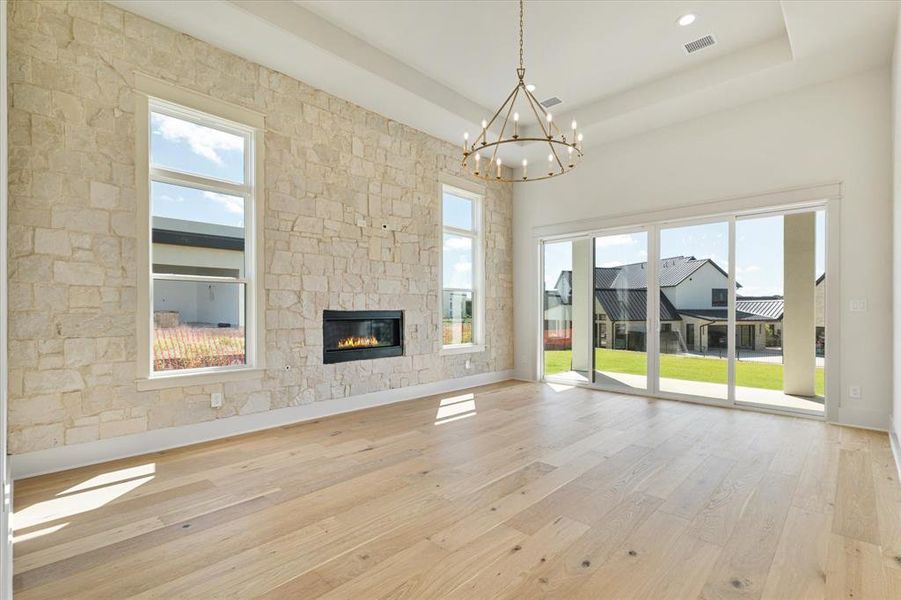 Unfurnished living room featuring a chandelier, light wood-style flooring, a stone fireplace, a raised ceiling, and recessed lighting