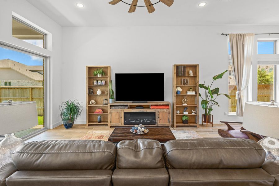 Bright, modern living room featuring large windows, wood tile floors, and a stylish ceiling fan. Natural light fills the space, offering a welcoming atmosphere.