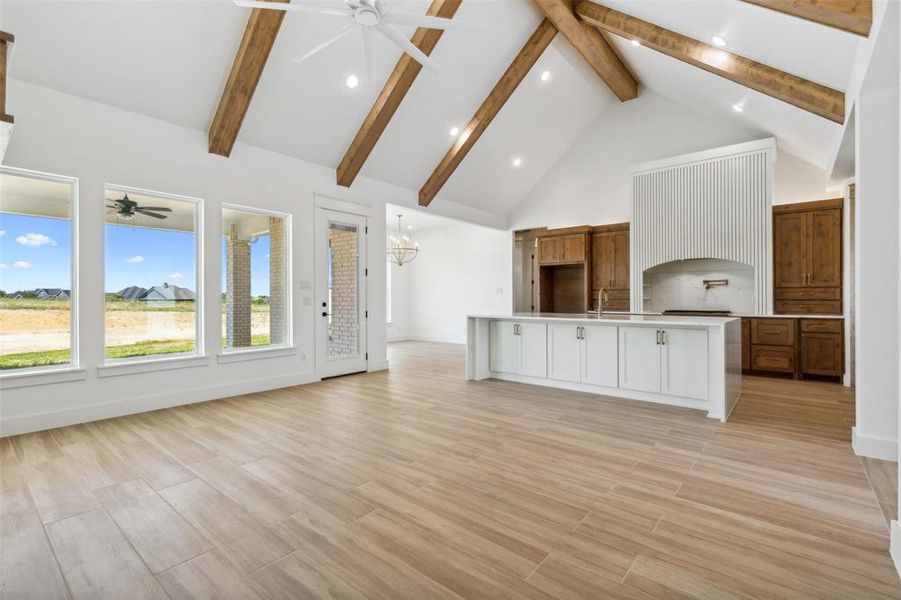 Unfurnished living room with light wood-type flooring, ceiling fan with notable chandelier, beamed ceiling, sink, and high vaulted ceiling