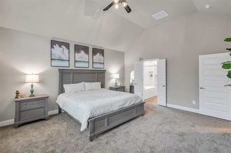 Bedroom featuring light carpet, ensuite bathroom, ceiling fan, and a high ceiling