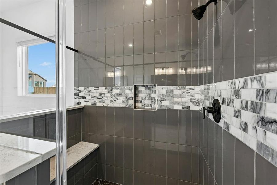 Shower enclosure featuring dark gray rectangular tile, a decorative marble-look mosaic band, a built-in shower bench, and a recessed shower niche