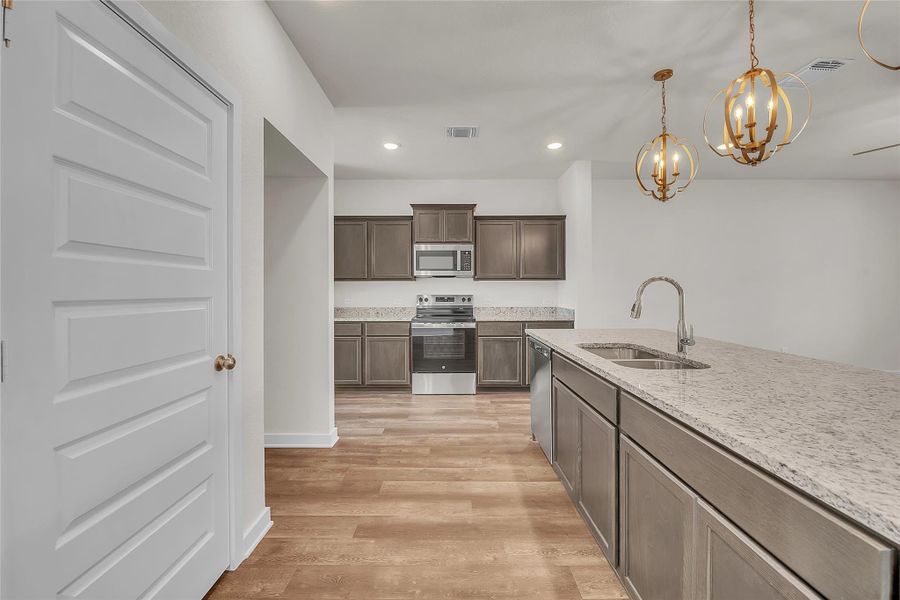Kitchen featuring appliances with stainless steel finishes, dark brown cabinetry, pendant lighting, recessed lighting, and a chandelier Kitchen featuring appliances with stainless steel finishes, dark brown cabinetry, pendant lighting, recessed lighting, and a chandelier