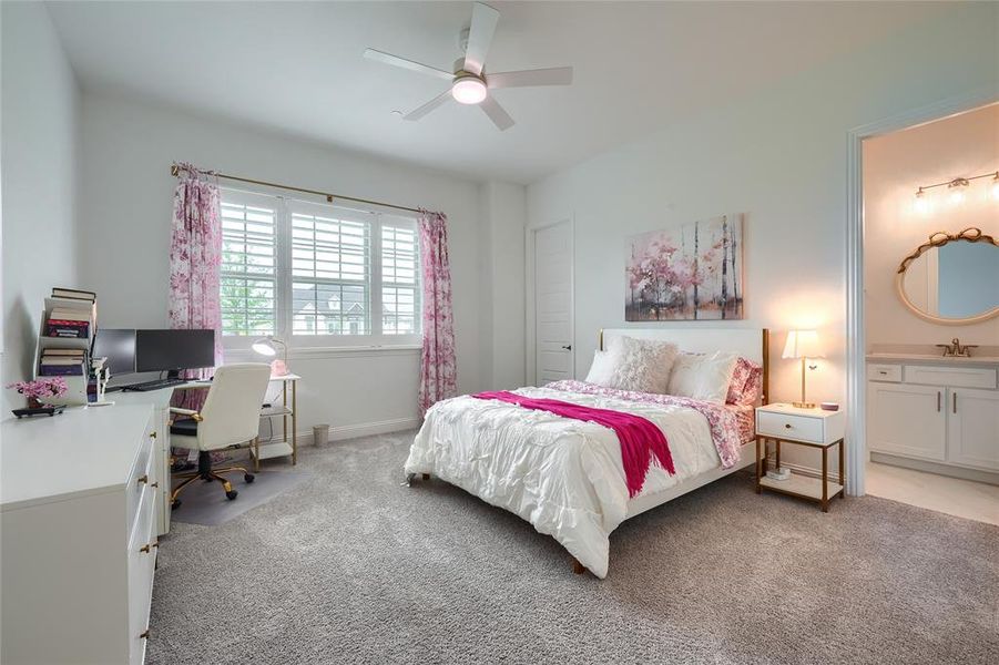 Bedroom featuring light colored carpet, an office area, ensuite bathroom, and a ceiling fan