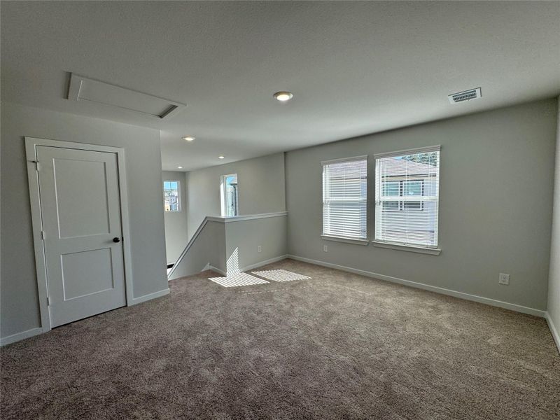 Bright, carpeted upstairs game room featuring ample natural light from multiple windows, recessed lighting, and a neutral color palette. The open layout provides flexible use as a game room, media space, or secondary living area. Bright, carpeted upstairs game room featuring ample natural light from multiple windows, recessed lighting, and a neutral color palette. The open layout provides flexible use as a game room, media space, or secondary living area.