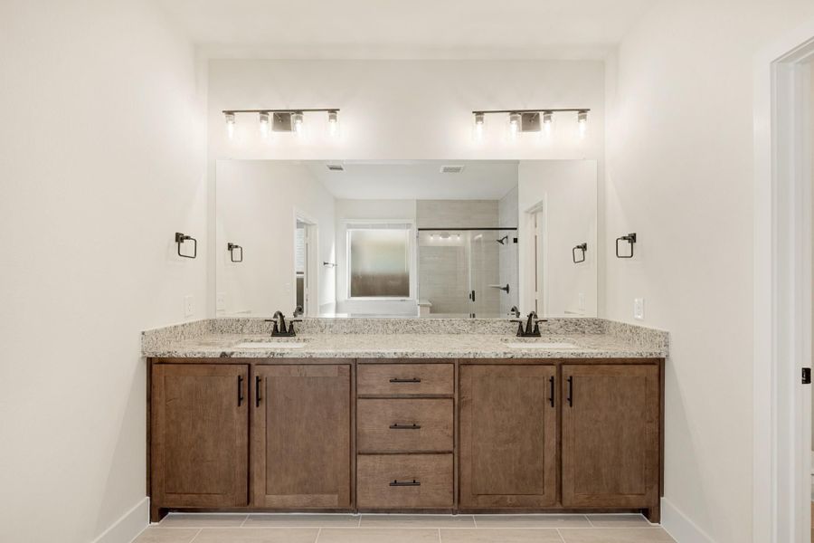 Bathroom double vanity with wood cabinets, granite countertop, dual sinks, and large mirror with overhead lighting