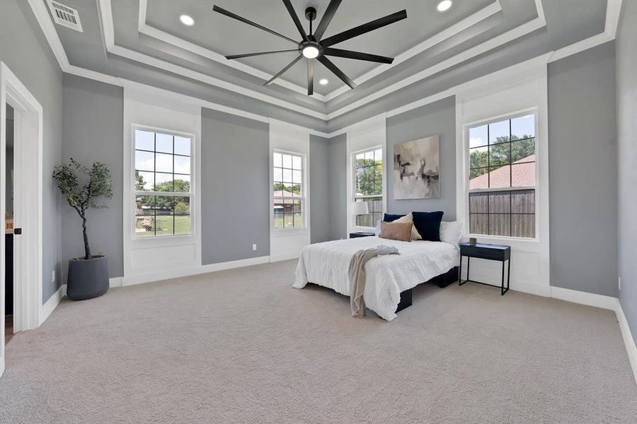 Spacious room featuring multiple windows, recessed lighting, a tray ceiling with crown molding, a large ceiling fan, and light-colored carpeting