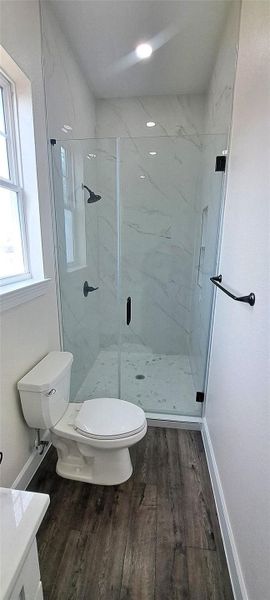 Full bath with a marble finish shower, vanity, and dark wood-style floors