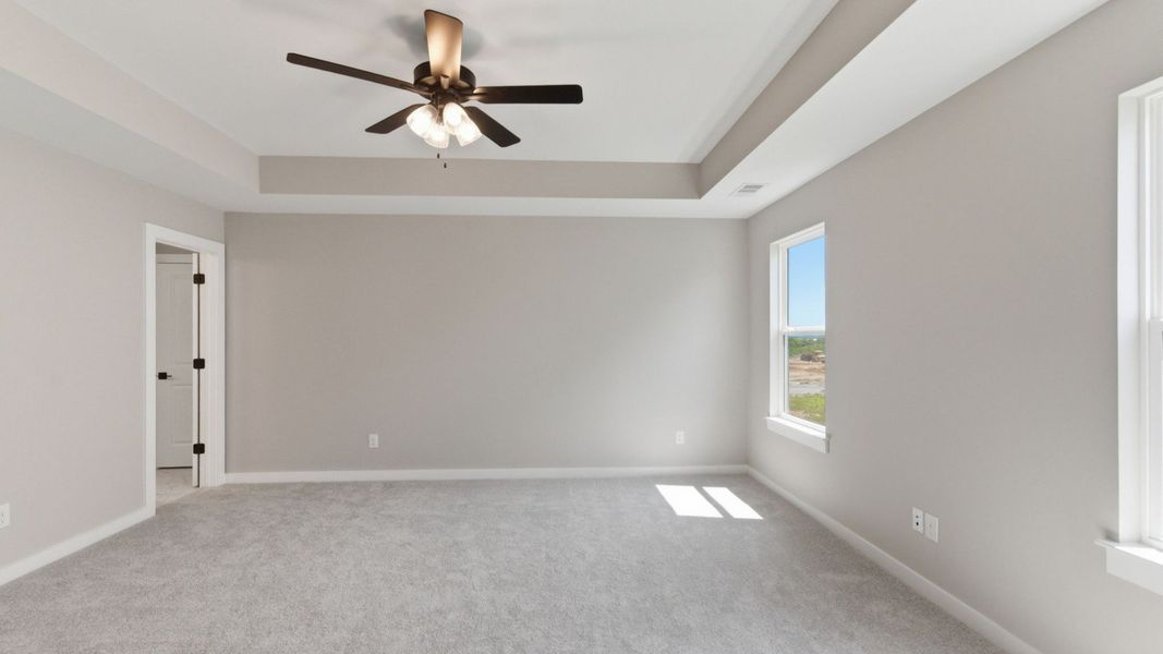 Primary suite with tray ceiling, ceiling fan, and carpet Primary suite with tray ceiling, ceiling fan, and carpet