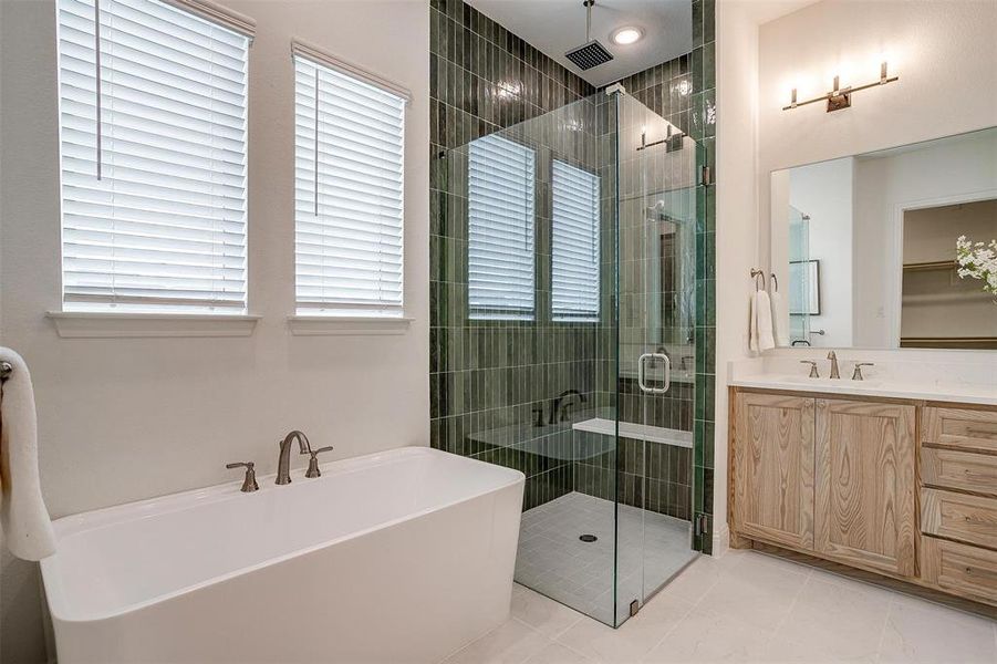 Bathroom with vanity, walk in shower with standard shower head and rain head, freestanding bathtub, and beautiful green tile that compliments the natural stained cabinets.