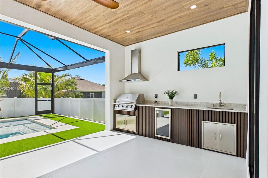 Outdoor kitchen is fully equipped w/ grill, hood vent, mini refrigerator & commercial-grade sink