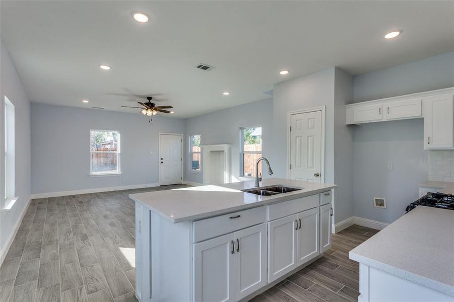 Kitchen with white cabinets, an island with sink, ceiling fan, and sink