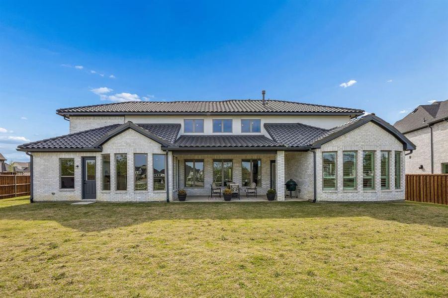 Rear view of house with a fenced backyard, a patio, brick siding, and a tiled roof