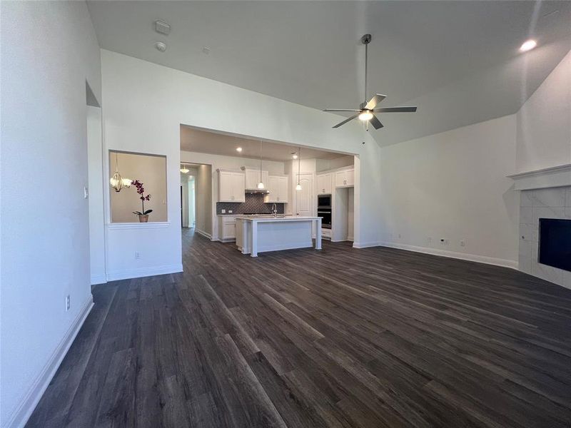 Living room with ceiling fan, high vaulted ceiling, a tile fireplace, dark wood-style flooring, and baseboards