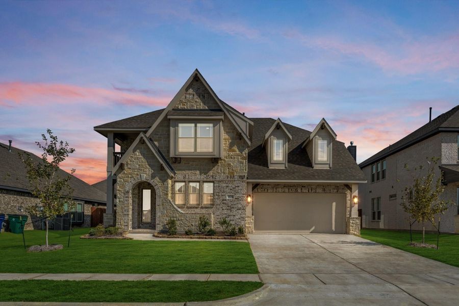 Two-story stone and brick home with arched entry, two-car garage, and green front lawn at dusk