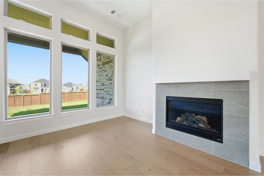 Living area featuring a gas fireplace with a tiled surround, wood-finish flooring, and a series of tall windows