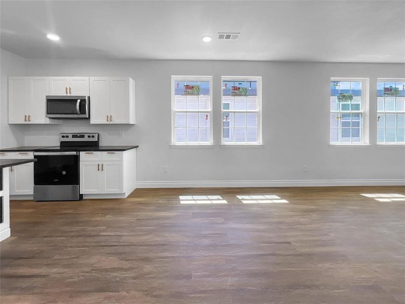Kitchen featuring stainless steel appliances, dark wood-type flooring, dark countertops, white cabinetry, and open floor plan Kitchen featuring stainless steel appliances, dark wood-type flooring, dark countertops, white cabinetry, and open floor plan