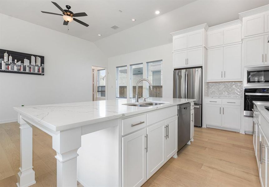 Kitchen with appliances with stainless steel finishes, white cabinets, tasteful backsplash, a center island with sink, and light wood finished floors Kitchen with appliances with stainless steel finishes, white cabinets, tasteful backsplash, a center island with sink, and light wood finished floors