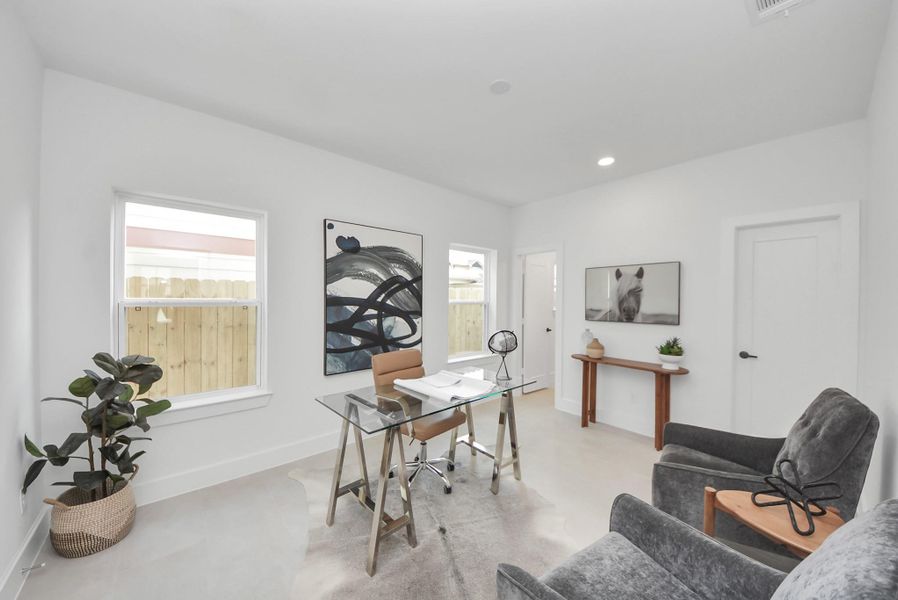 Step into this bright, modern home office, where a glass desk and comfortable seating are complemented by stylish artwork and minimalistic decor. Large windows fill the space with natural light, while neutral walls create an inviting and functional environment perfect for focused work or study.