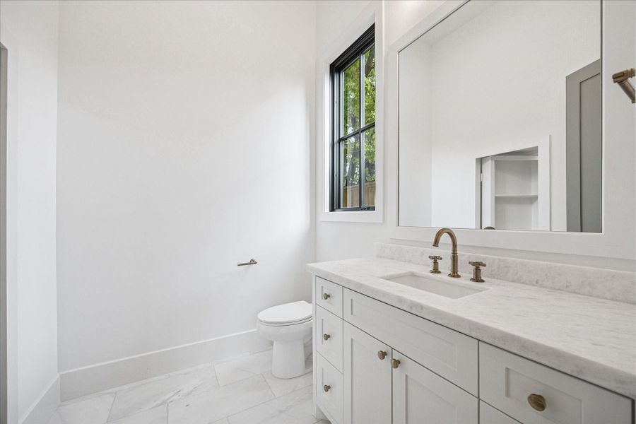 Soft natural light highlights marble counters, warm brass fixtures, and clean-lined cabinetry in the en-suite study bath. The spacious layout includes a frameless mirror and direct access to a concealed storage nook with custom shelving, ideal for keeping supplies tidy. High-efficiency windows and the insulated envelope enhance comfort year-round. *Previous Project*