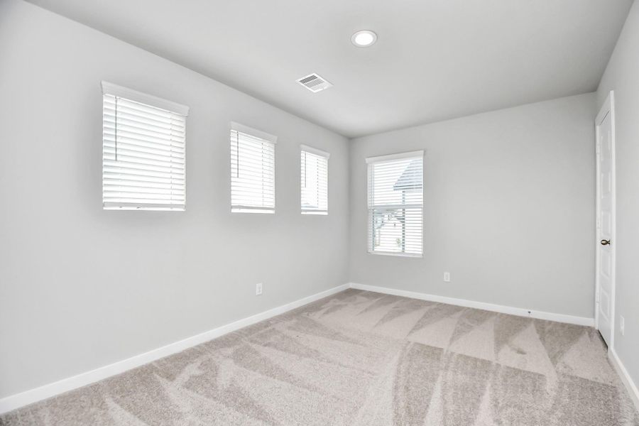Secondary bedroom features plush carpeting, large windows that let in plenty of natural light, bright paint, and spacious closets. Sample photo of completed home with similar floor plan. Actual colors and selections may vary.