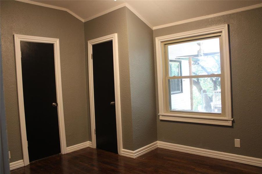 Unfurnished bedroom with a textured wall, dark wood-style flooring, and ornamental molding Unfurnished bedroom with a textured wall, dark wood-style flooring, and ornamental molding