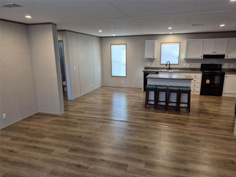 Kitchen featuring white cabinets, black appliances, a center island with sink, dark wood finished floors, and recessed lighting