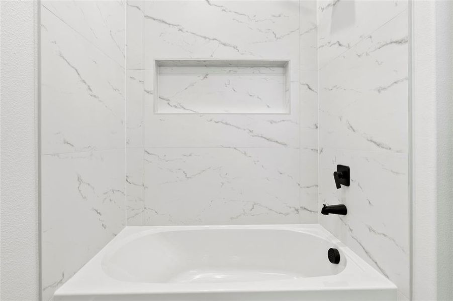 Bathtub with surrounding marble-patterned wall tile, featuring a recessed niche and matte black fixtures