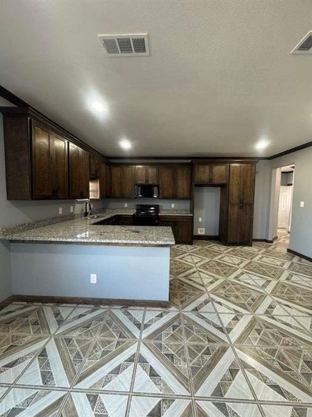 Kitchen with dark brown cabinets, a peninsula, light stone counters, and black appliances