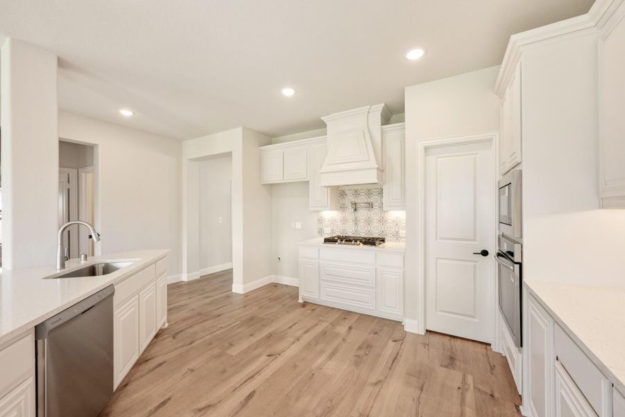 Kitchen with white cabinets, decorative range hood, patterned tile backsplash, and light wood floors