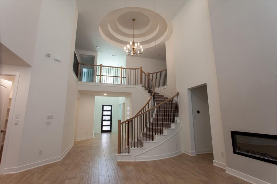 A breathtaking two-story foyer welcomes you with a sweeping curved staircase, dramatic circular tray ceiling, and a designer chandelier. A modern glass-paneled front door and built-in linear fireplace add unforgettable curb-to-interior impact.