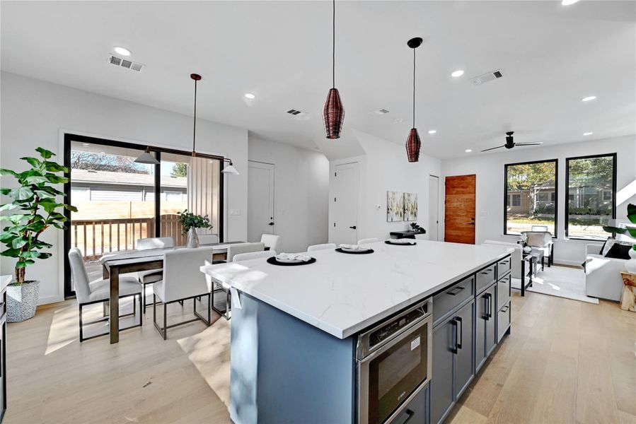 Kitchen with ceiling fan, decorative light fixtures, light stone countertops, a center island, and light hardwood / wood-style floors