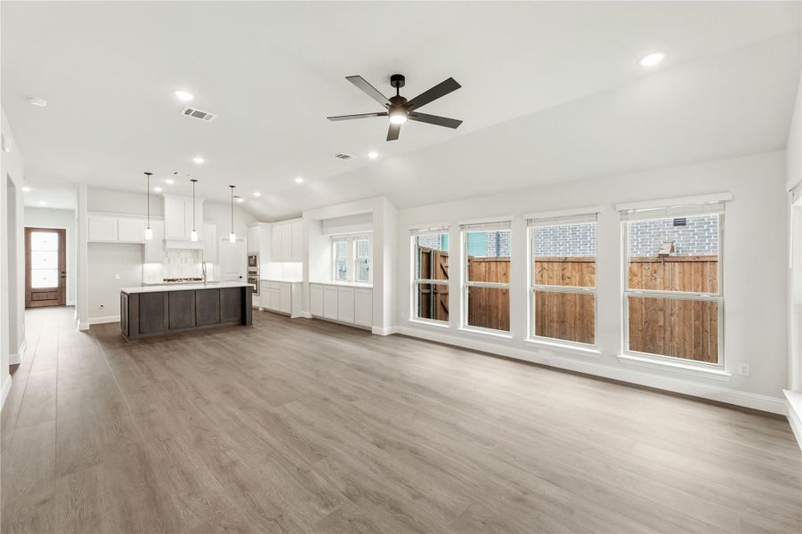 Open living area with hardwood floors and ceiling fan, open to kitchen with dark island and white cabinets Open living area with hardwood floors and ceiling fan, open to kitchen with dark island and white cabinets