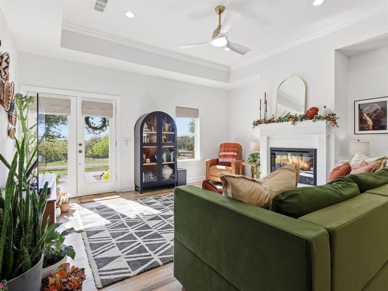 Living room with wood finished floors, a glass covered fireplace, french doors, ornamental molding, and recessed lighting