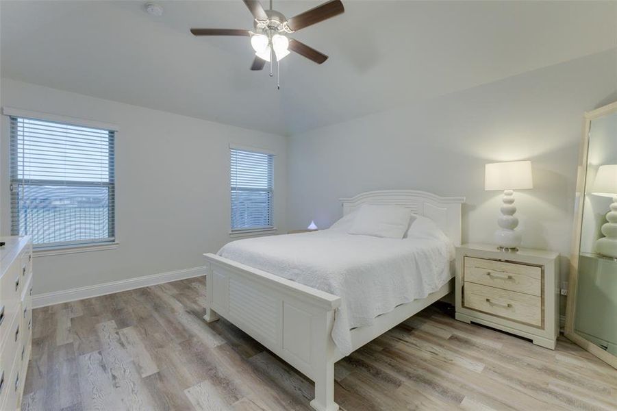 Bedroom featuring light wood-type flooring, vaulted ceiling, multiple windows, and ceiling fan